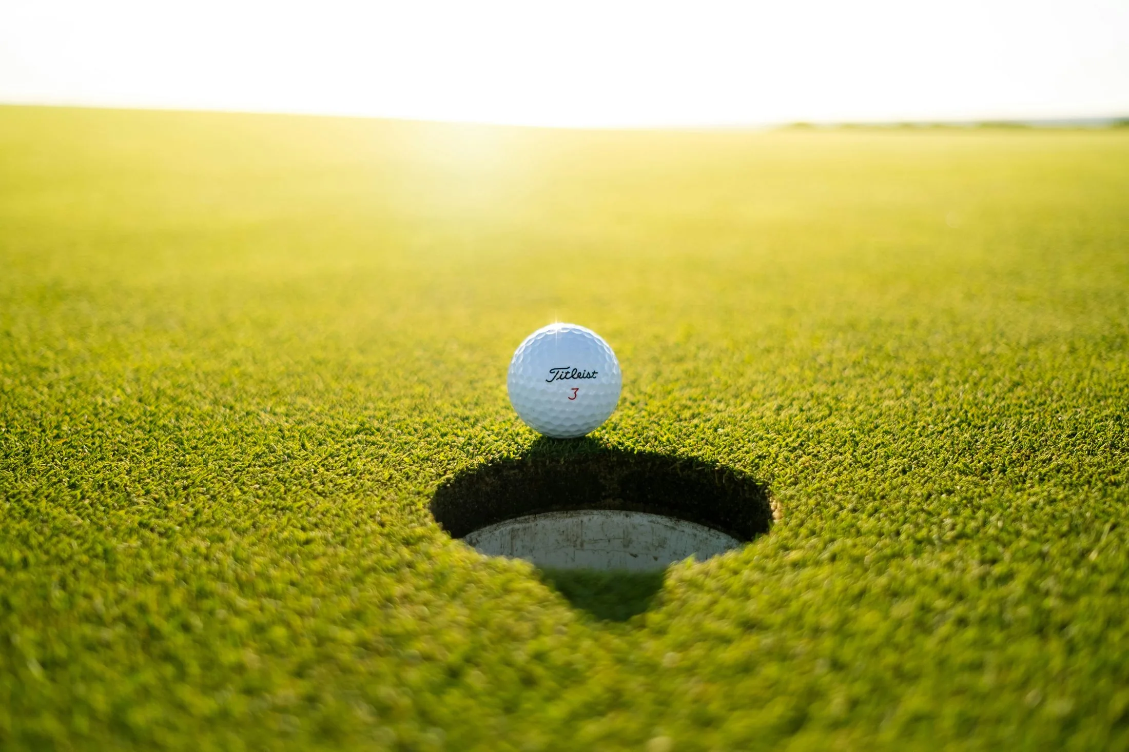 A golf ball settling at the lip of the cup