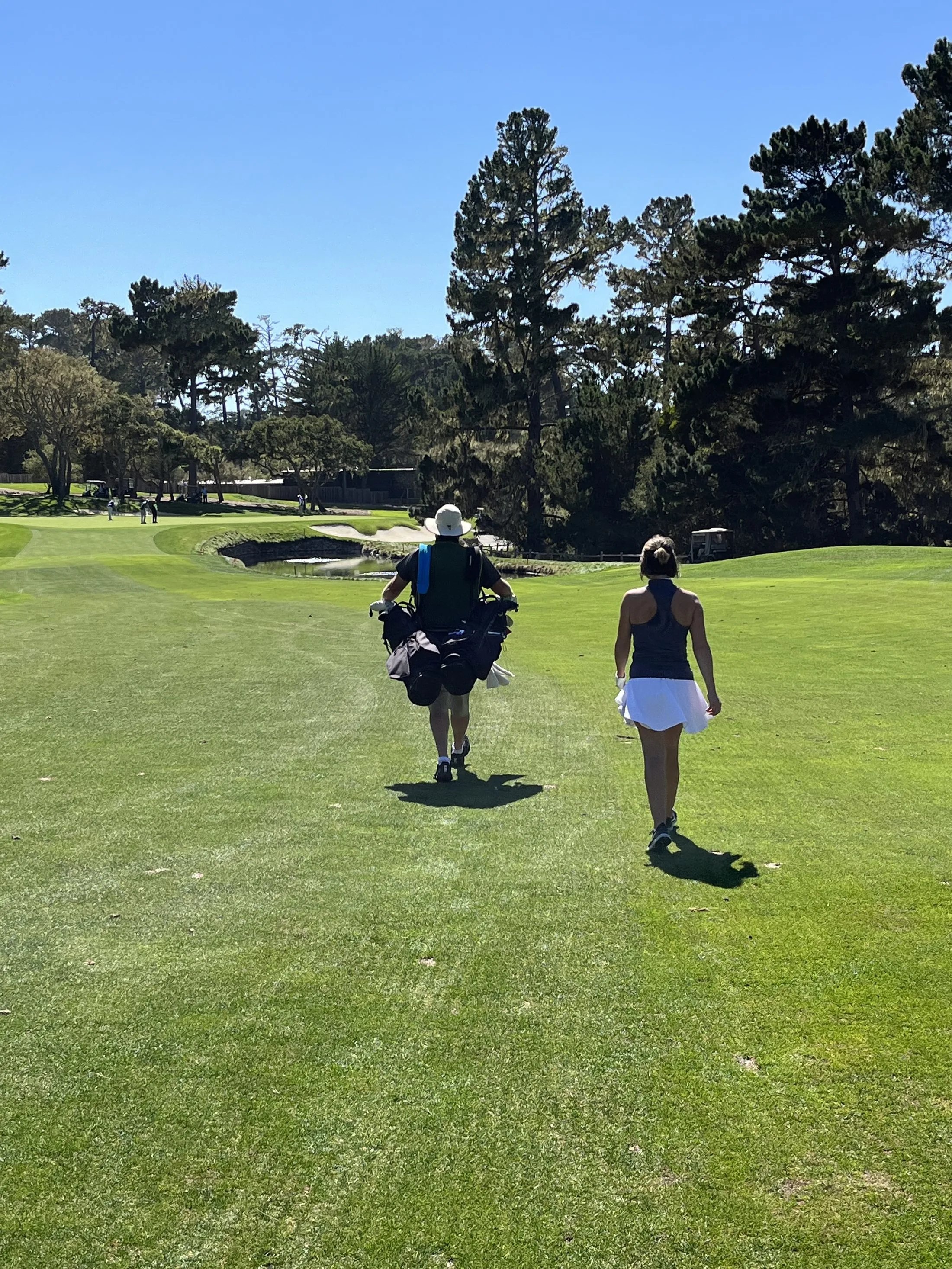 A woman walking down the fairway with her caddy